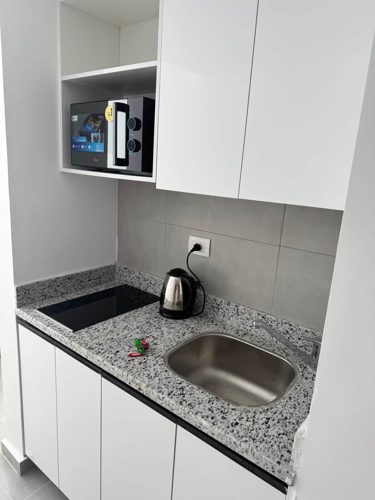 Una cocina con estufa integrada, hervidor y pileta de acero inoxidable.