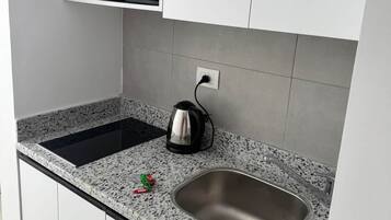 Una cocina con estufa integrada, hervidor y pileta de acero inoxidable.