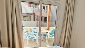 Hotellihuone, jossa on sänky, lasioven kautta näkyvä ulkoalue, jossa on istuimia, sekä verhot.