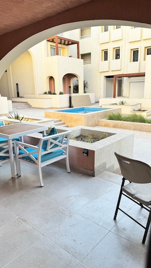 Ein Außenbereich mit Sitzgelegenheiten, einem Pool, einer überdachten Terrasse und Blick auf ein Wohngebäude.