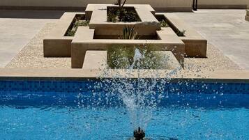 A swimming pool with a fountain feature, surrounded by a geometric planter with plants.
