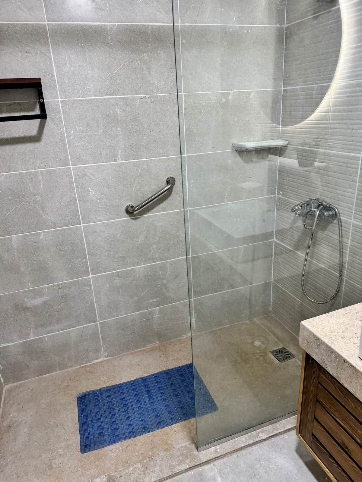 Een douche met een glazen deur, een handgreep en een handdouche.