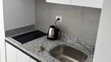 Una cocina con un lavamanos de acero inoxidable, una tetera y una estufa empotrada.