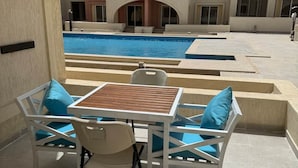 Un espace aménagé au bord de la piscine, avec une table et des chaises, une piscine, et un bâtiment avec des balcons en arrière-plan.