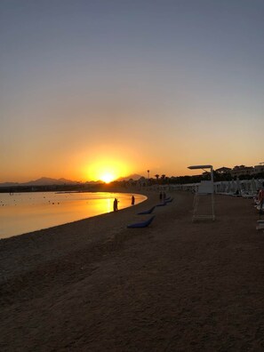 Ein Strand mit Sonnenuntergang, ruhigem Wasser und einer Reihe von Liegestühlen.