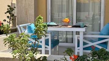 Eine Terrasse mit Tisch und Stühlen, einem Blumentopf und Blick durch ein Fenster.