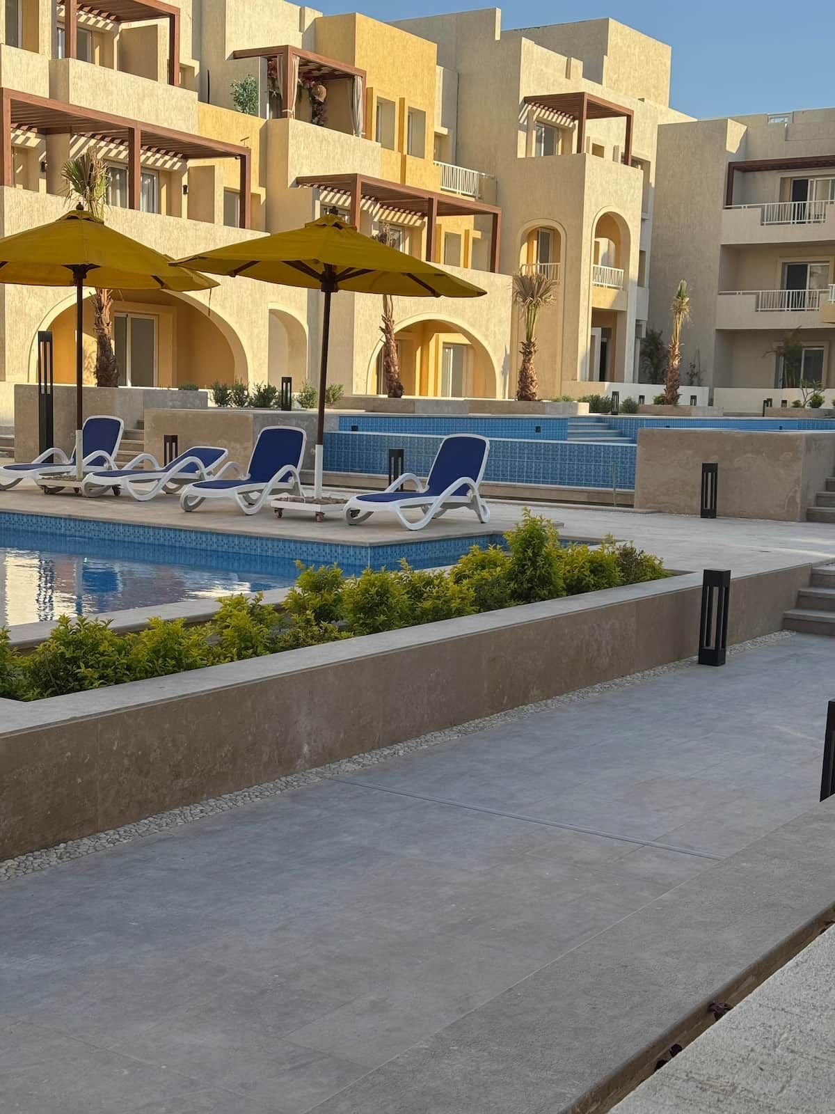 Ein Poolbereich mit Liegestühlen und Sonnenschirmen, umgeben von einem Gebäude mit Balkonen und einem mit Fliesen ausgelegten Pool.