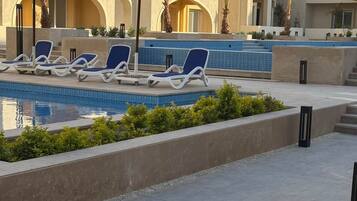 Ein Poolbereich mit Liegestühlen und Sonnenschirmen, umgeben von einem Gebäude mit Balkonen und einem mit Fliesen ausgelegten Pool.