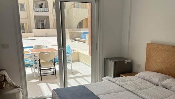 Une chambre avec un lit, une table de chevet, une chaise et une vue sur un espace extérieur accessible par une porte-fenêtre coulissante, cet espace comprenant une piscine et des sièges.