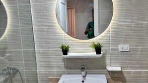 Une salle de bain avec un lavabo rectangulaire, un miroir rond et un espace douche.