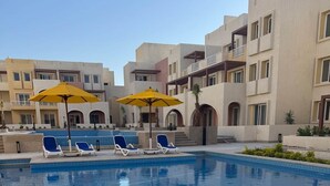 Une piscine entourée d’immeubles à plusieurs étages, avec des chaises longues et des parasols.