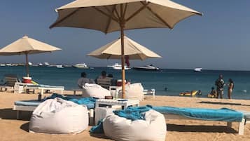 Ein Strand mit Liegestühlen, Sonnenschirmen und einem Sandbereich mit Blick auf das Meer und Boote.