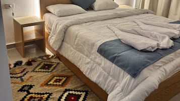 Un dormitorio con cama, mesita de noche y una alfombra estampada.