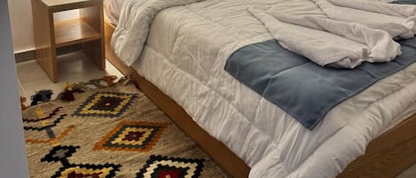 A bedroom with a bed, nightstand, and a patterned rug.