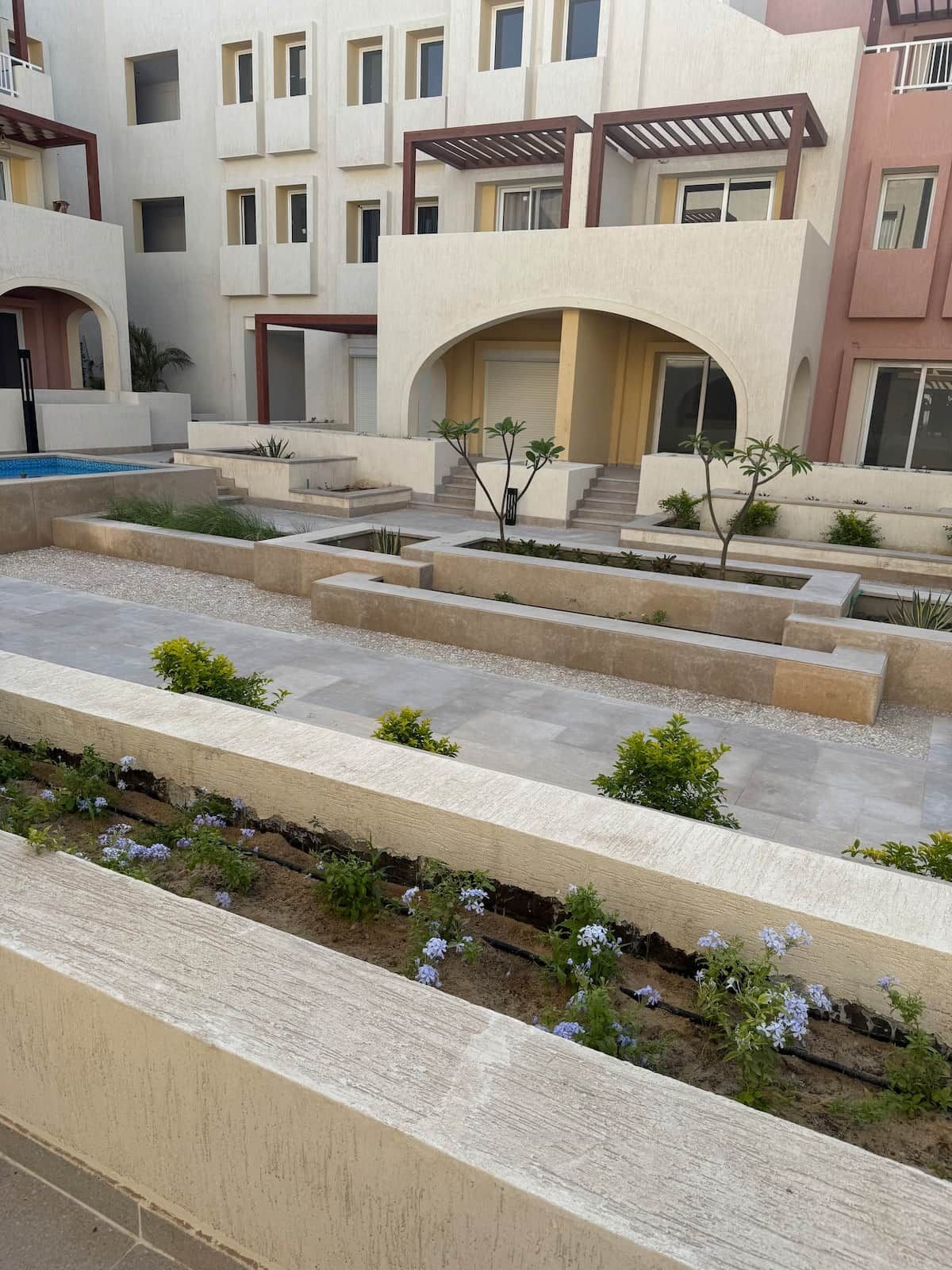 Un edificio moderno con varios balcones, un patio central con plantas y una piscina.