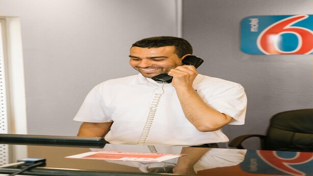 En person sitter vid ett skrivbord med en telefon, ett anteckningsblock och en vägg med en nummersymbol på.
