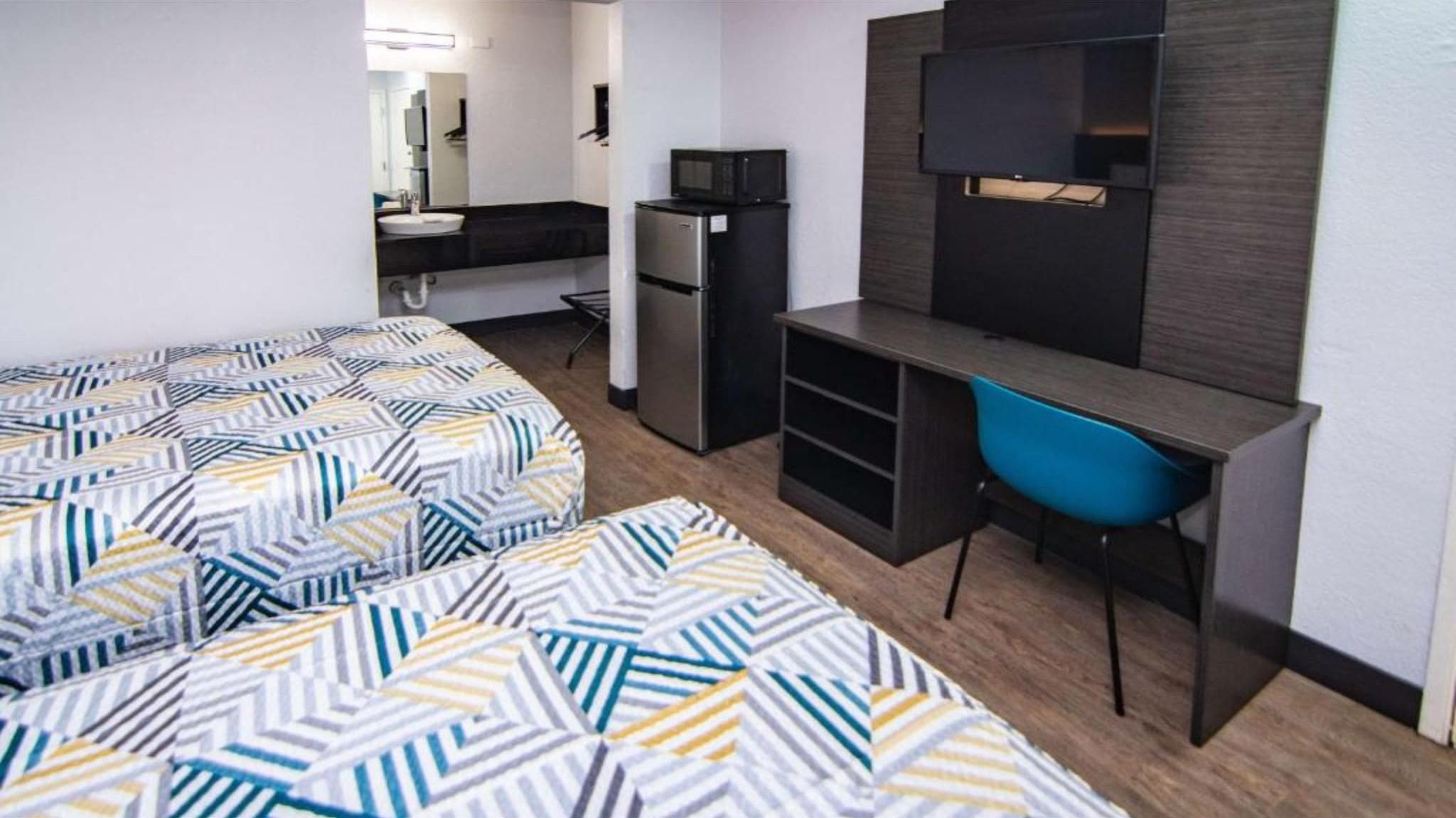 Habitación de hotel compacta con dos camas, kitchenette, escritorio con silla y televisión.