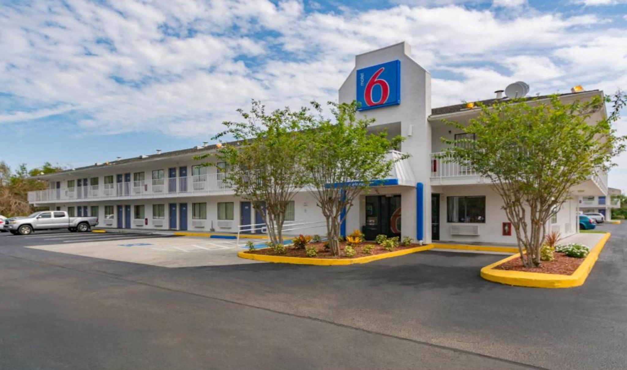 Un motel con un letrero que indica el número '6', un estacionamiento y un edificio con varias ventanas y balcones.