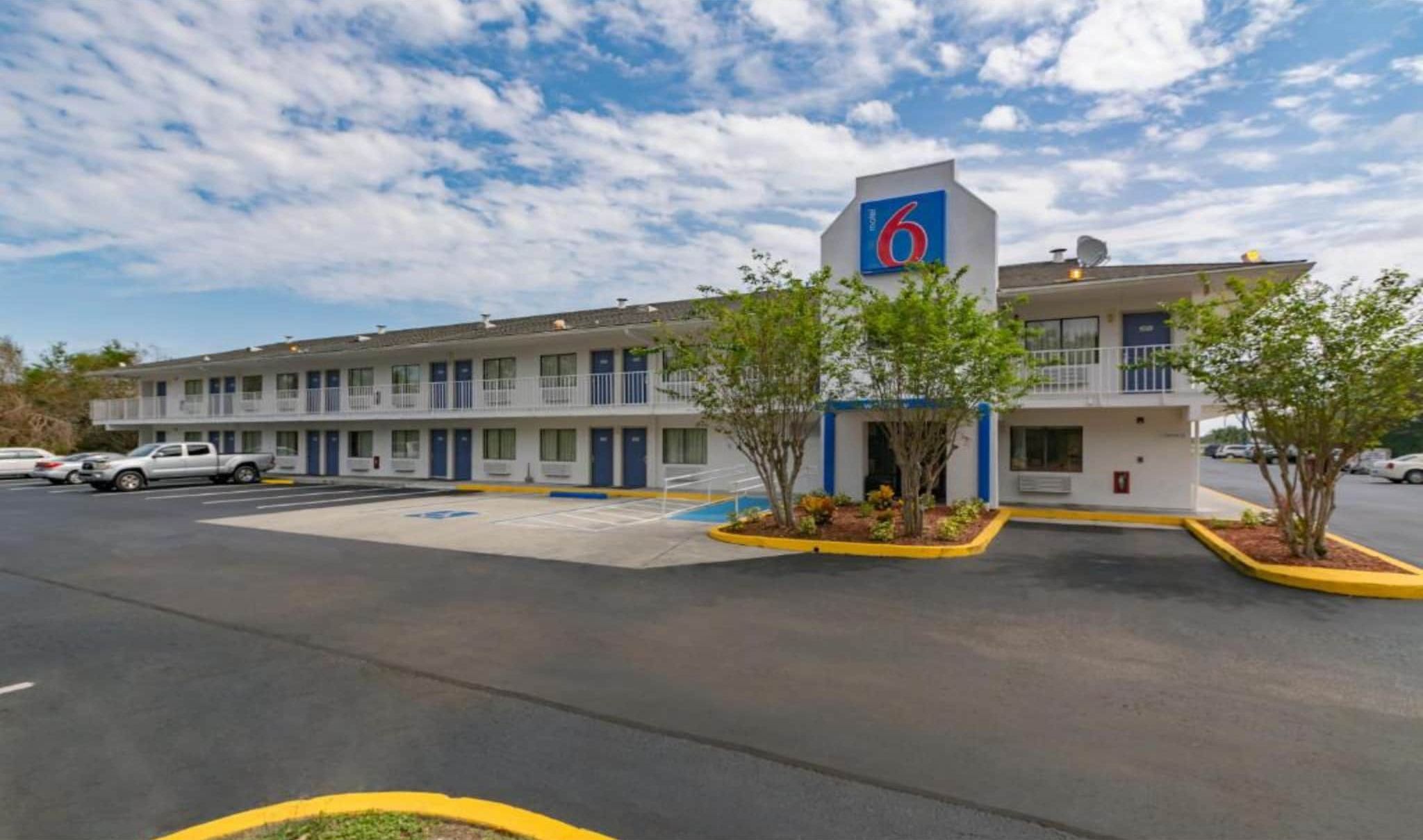 Een motel met een bordje met 6 kamers, een parkeerplaats en een klein aangelegd gebied met bomen.