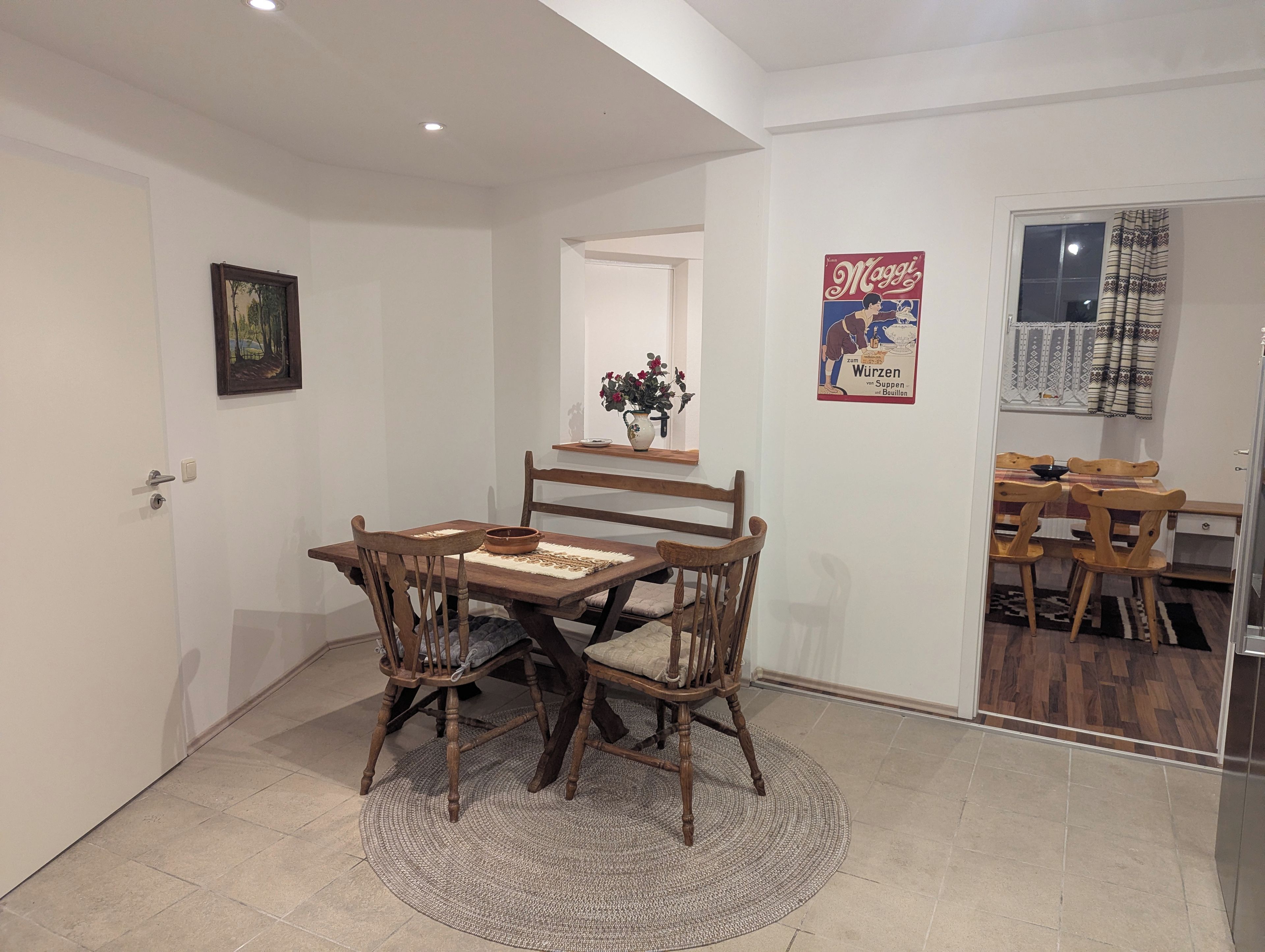 Un comedor con una mesa y sillas de madera, una alfombra y un cartel en la pared.