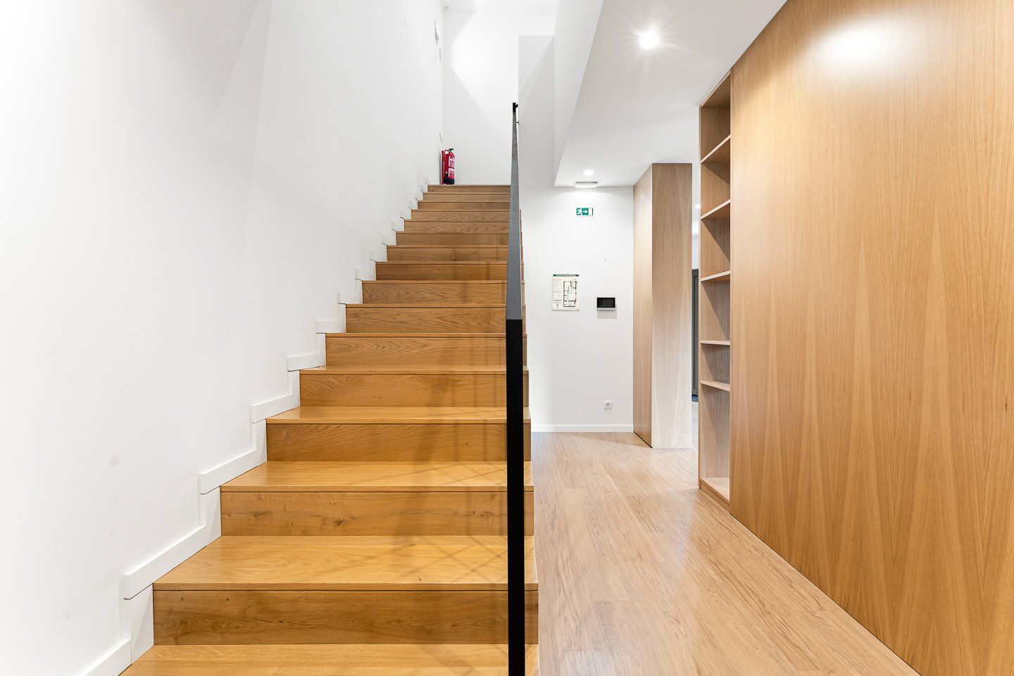 A staircase with wooden steps leading to a landing, flanked by white walls and a wooden panel on the right.