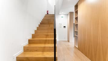 Una escalera con escalones de madera que conduce a una plataforma, flanqueada por paredes blancas y un panel de madera a la derecha.