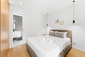 A modern hotel room with a large bed, a wooden door, a bathroom with grey tiles, and a small bedside table. - Guestready - Poetikblue Residences (Porto)