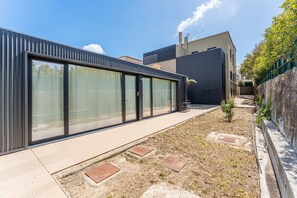 A modern building with large glass windows, a concrete pathway, and a small garden area with a palm tree. - Guestready - Poetikblue Residences (Porto)