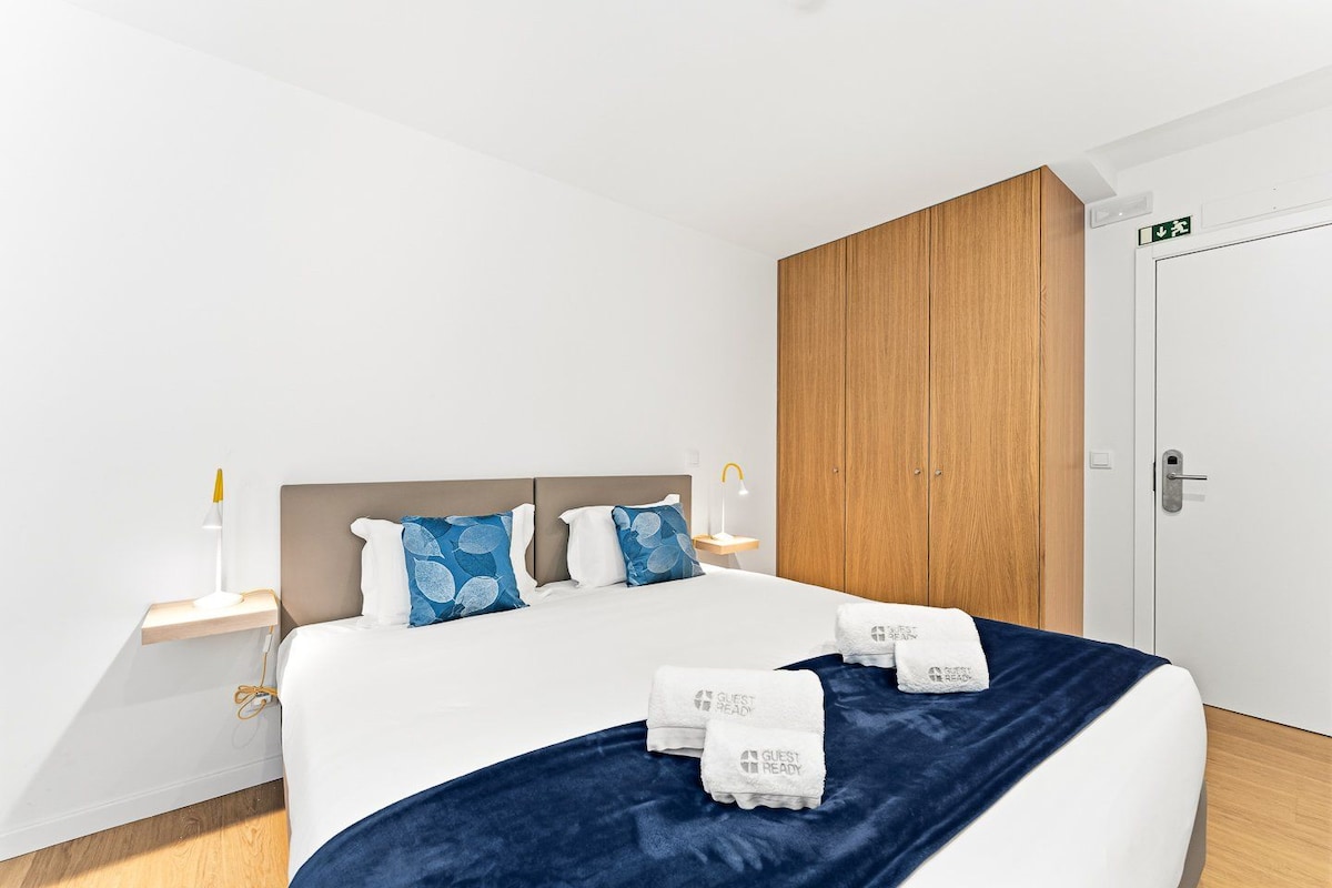 A hotel room with a bed, bedside tables, a wardrobe, and a door with an exit sign.