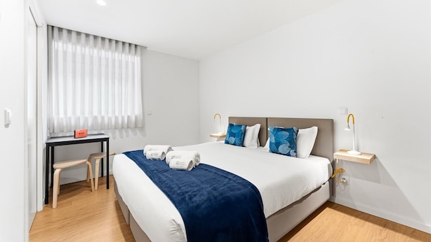 A hotel room with a bed, bedside tables, a desk, and a chair. - Guestready - Poetikblue Residences (Porto)