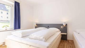 Un dormitorio con cama, mesita de noche, ventana con cortinas y vista a edificios.