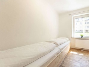 Una cama individual con estructura de madera y ropa de cama blanca en una habitación con ventana.