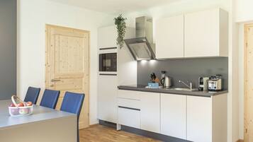 A compact kitchen with white cabinets, a microwave, a sink, and a toaster. There is a wooden door and a plant on the wall.