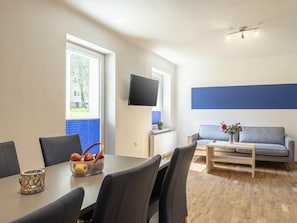 Una sala de estar moderna con comedor, un televisor de pantalla plana montado en la pared, un sofá con un jarrón de flores y piso de madera.
