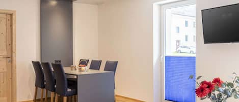 A modern dining area with a table and chairs, a television mounted on the wall, and a window with blinds.