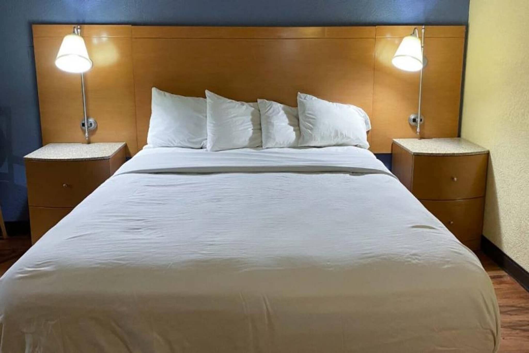 A hotel room with a large bed, two bedside tables, and two wall-mounted lamps.