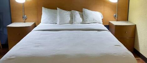 A hotel room with a large bed, two bedside tables, and two wall-mounted lamps.