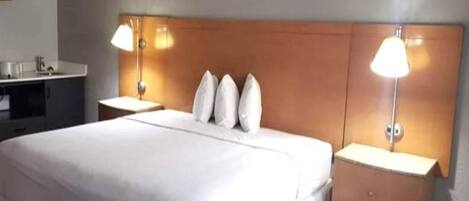 Una habitación de hotel con una cama grande, dos mesitas de noche y dos lámparas fijadas a la pared.