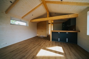 A room with wooden floors, a sloped ceiling, a window, and a kitchenette area.