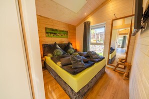 A bedroom with a bed, wooden walls, a painting, and a view through a window.