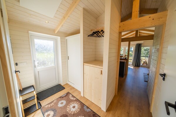 A wooden interior with a door, a coat rack, and a view to the outside.