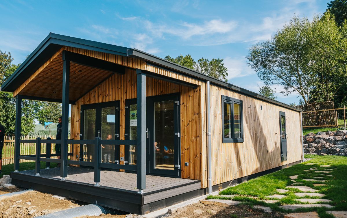 Een moderne houten blokhut met een overdekte veranda, grote ramen en een pad van stenen.