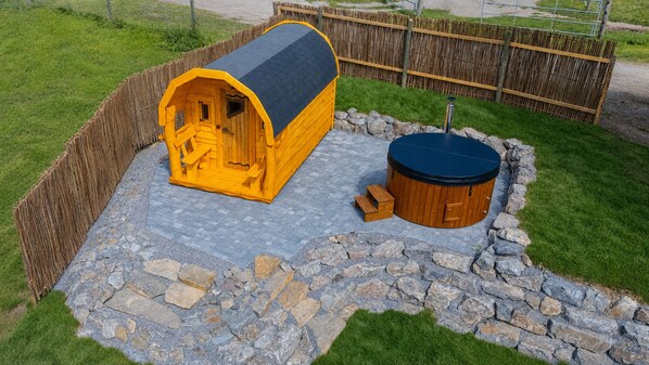 A wooden cabin with a black roof, a stone pathway, and a hot tub.