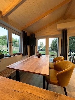 A dining area with a wooden table and yellow chairs, large windows, and a view of the outdoors.