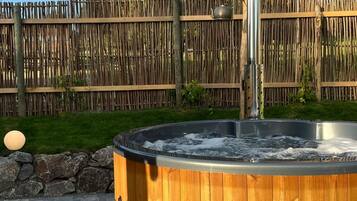 A hot tub with a wooden exterior, a metal pole, and a stone wall in the background.