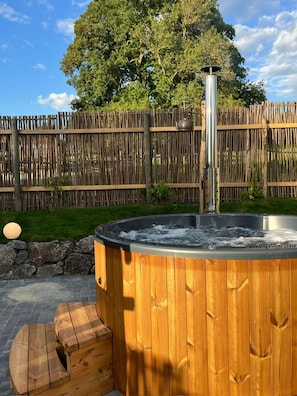 A hot tub with a wooden exterior, a metal pole, and a stone wall in the background.