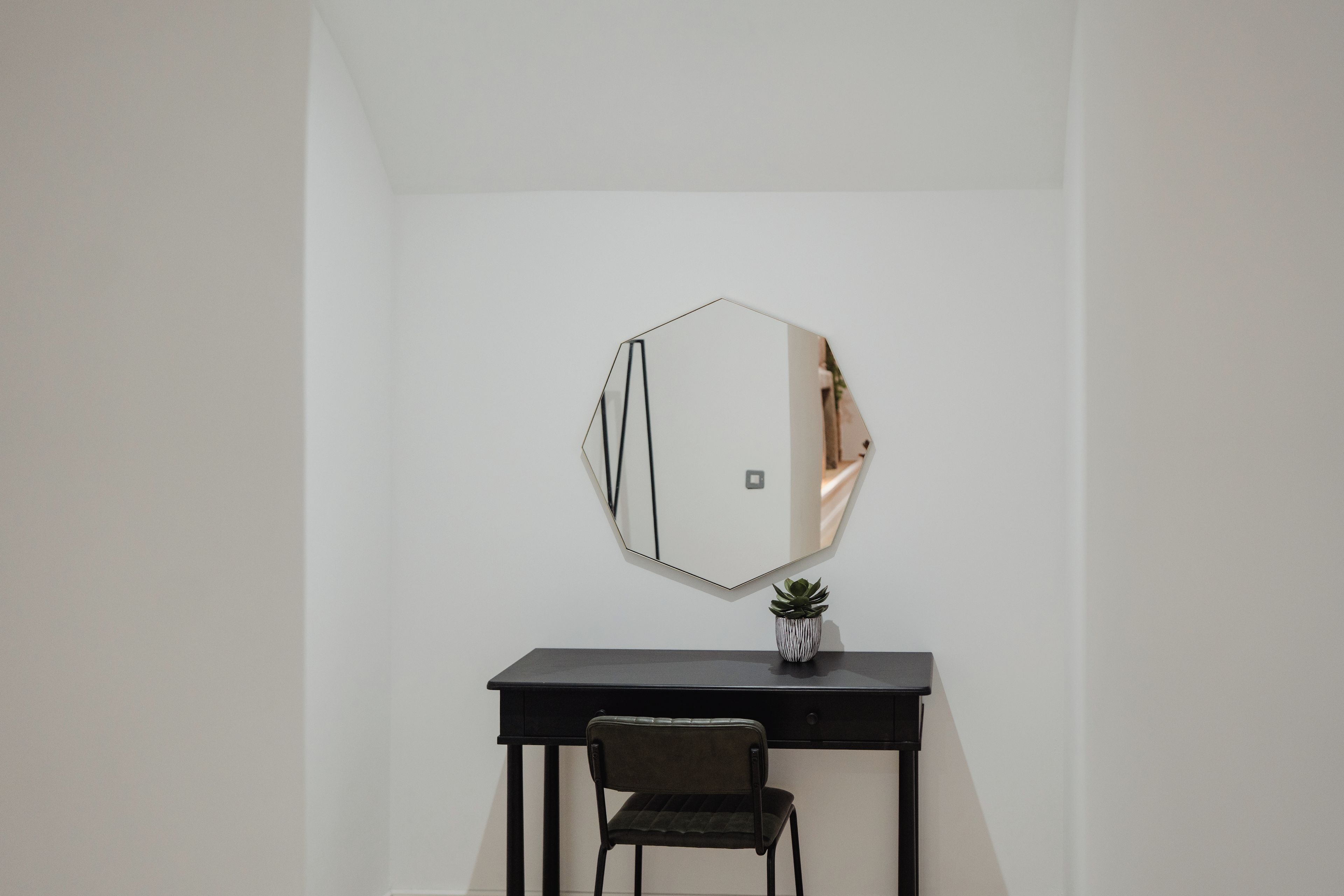 Une pièce avec un bureau noir, une chaise et un miroir fixé au mur.