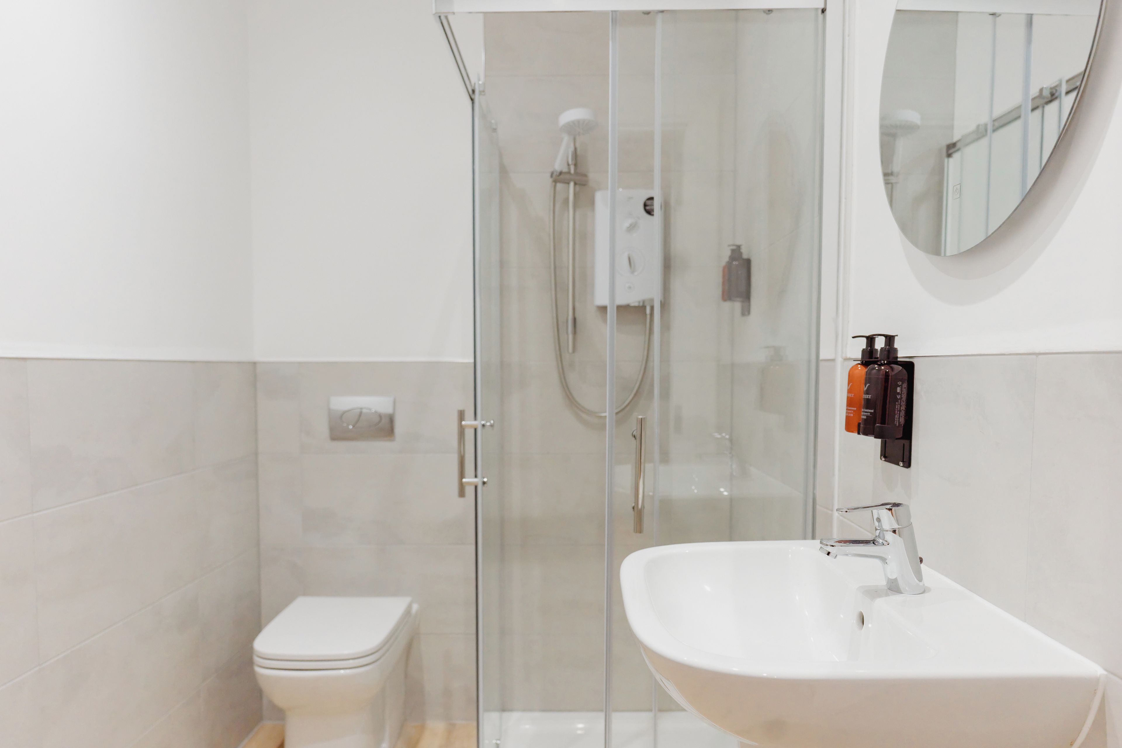 A modern bathroom with a glass-enclosed shower, a white toilet, and a sink with a mirror above.