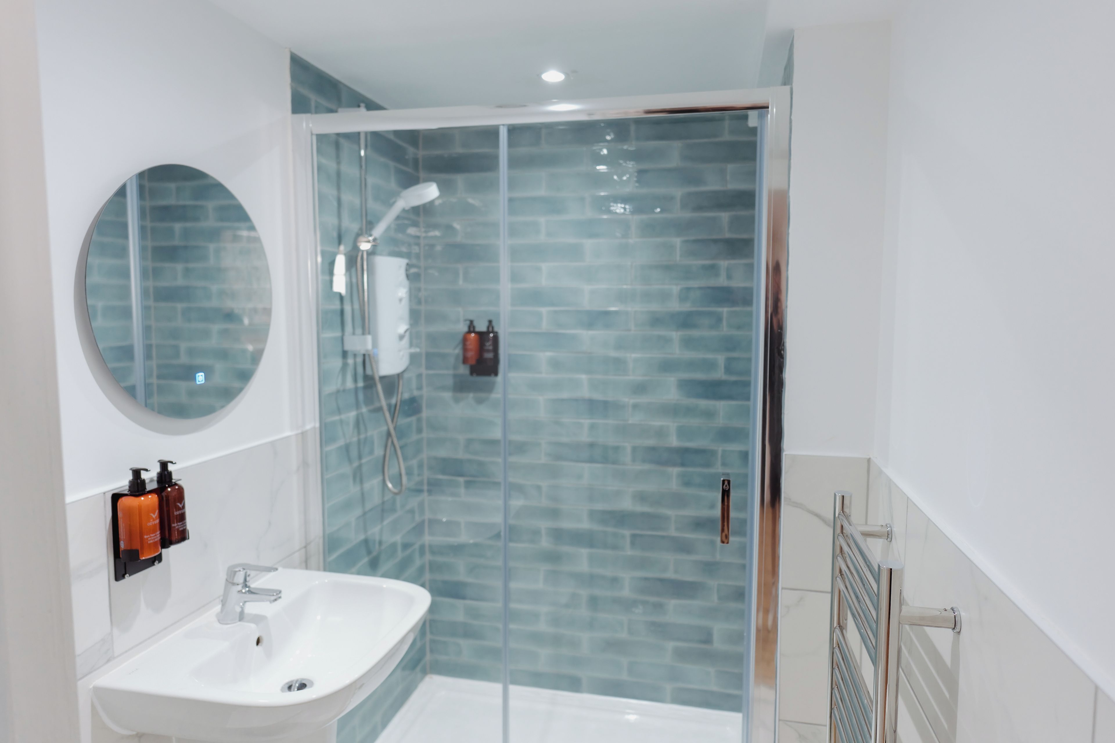 A modern bathroom with a glass-enclosed shower, a white sink, and a round mirror.