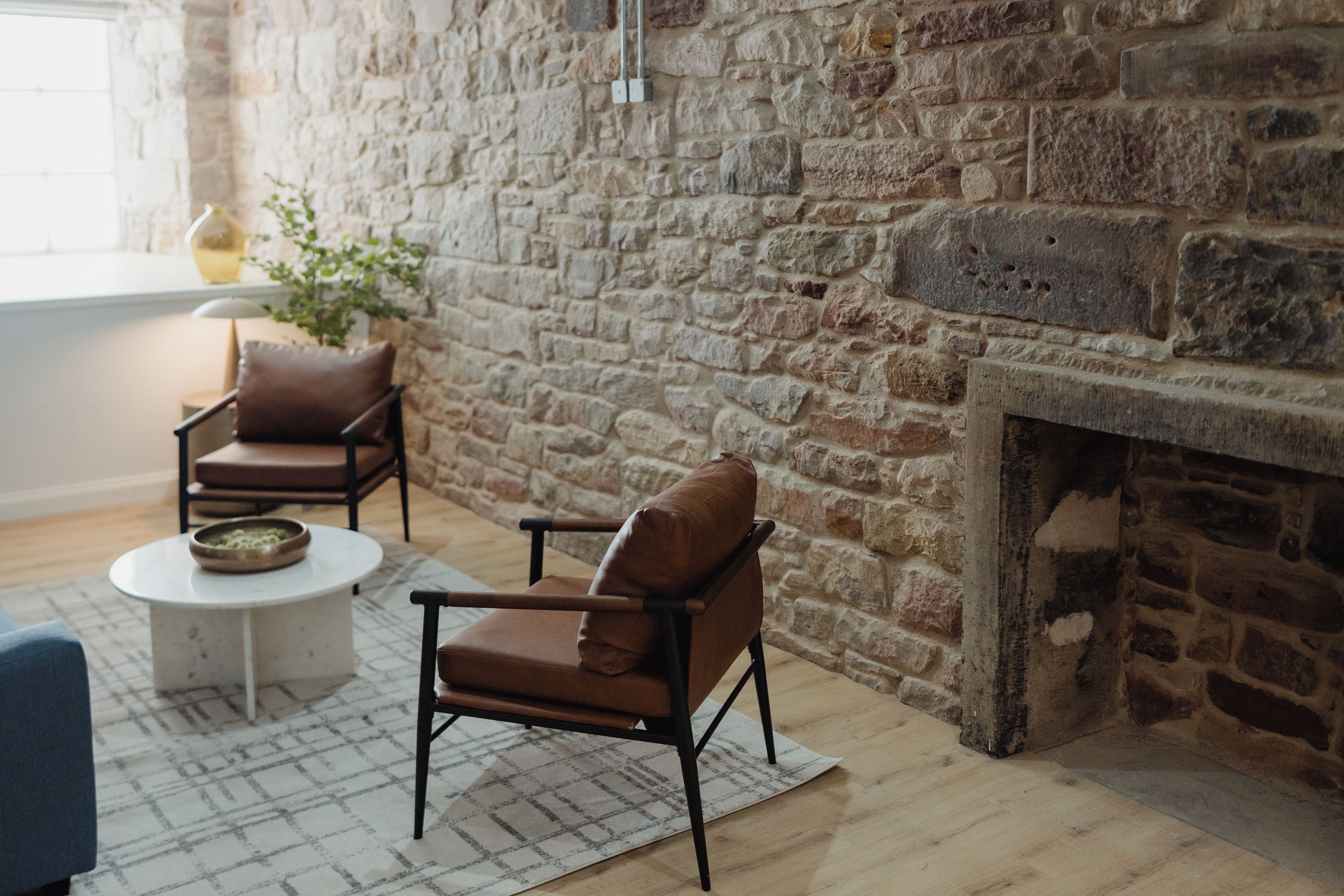 A room with a stone wall, a fireplace, two leather chairs, a small round table, and a blue sofa.